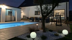 A modern house with a swimming pool, outdoor seating, and a well-lit patio area.