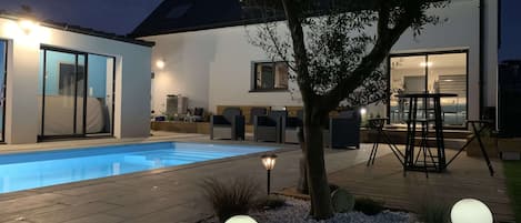A modern house with a swimming pool, outdoor seating, and a well-lit patio area.