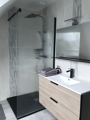 A modern bathroom with a glass shower enclosure, a white sink, and a wooden vanity.