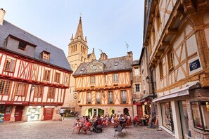 A historic European town square with half-timbered buildings, a church tower, and outdoor seating areas.