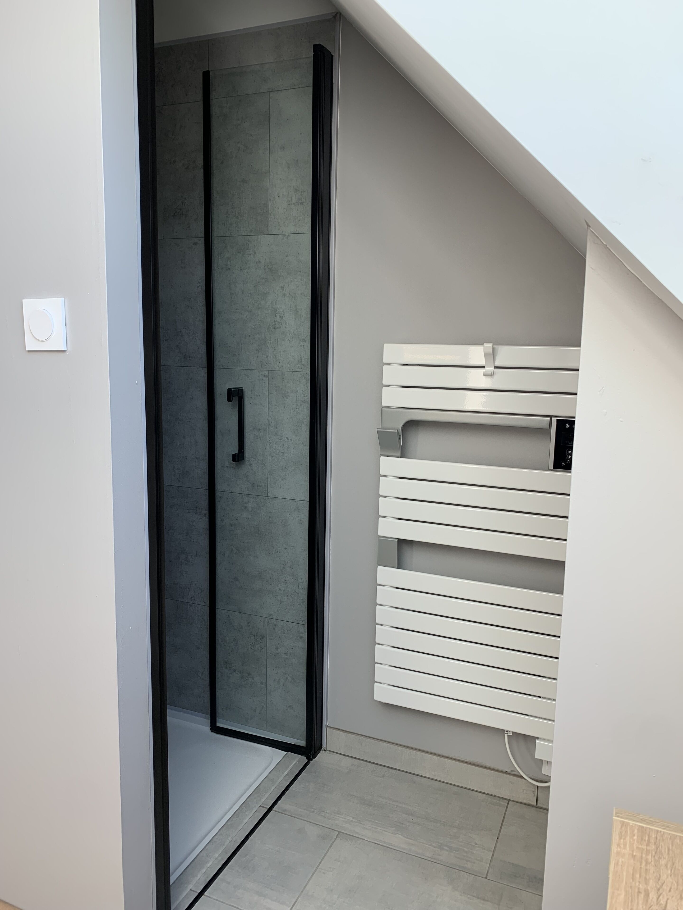 Un baño moderno con mampara de vidrio, toallero blanco y suelo de baldosas grises.