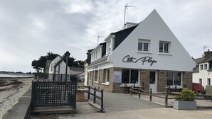 A coastal building named "Cote Plage" with a prominent sign, a terrace with seating, and a view of the beach.