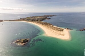 An aerial view of a coastal area with a sandy beach, clear waters, and a small island.