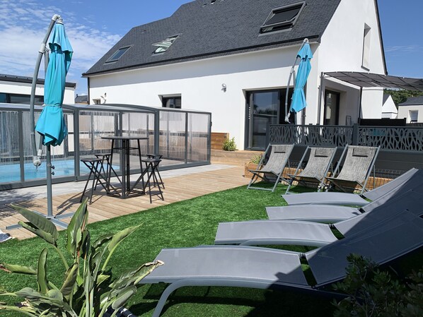 A modern outdoor patio with a pool, sun loungers, and a covered seating area.
