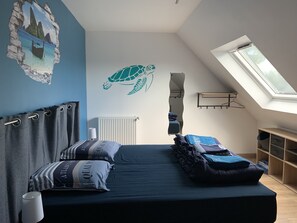 A bedroom with a sloped ceiling, a skylight, a bed with striped bedding, a wall mural of a sea turtle, and a view of a wooden shelf.