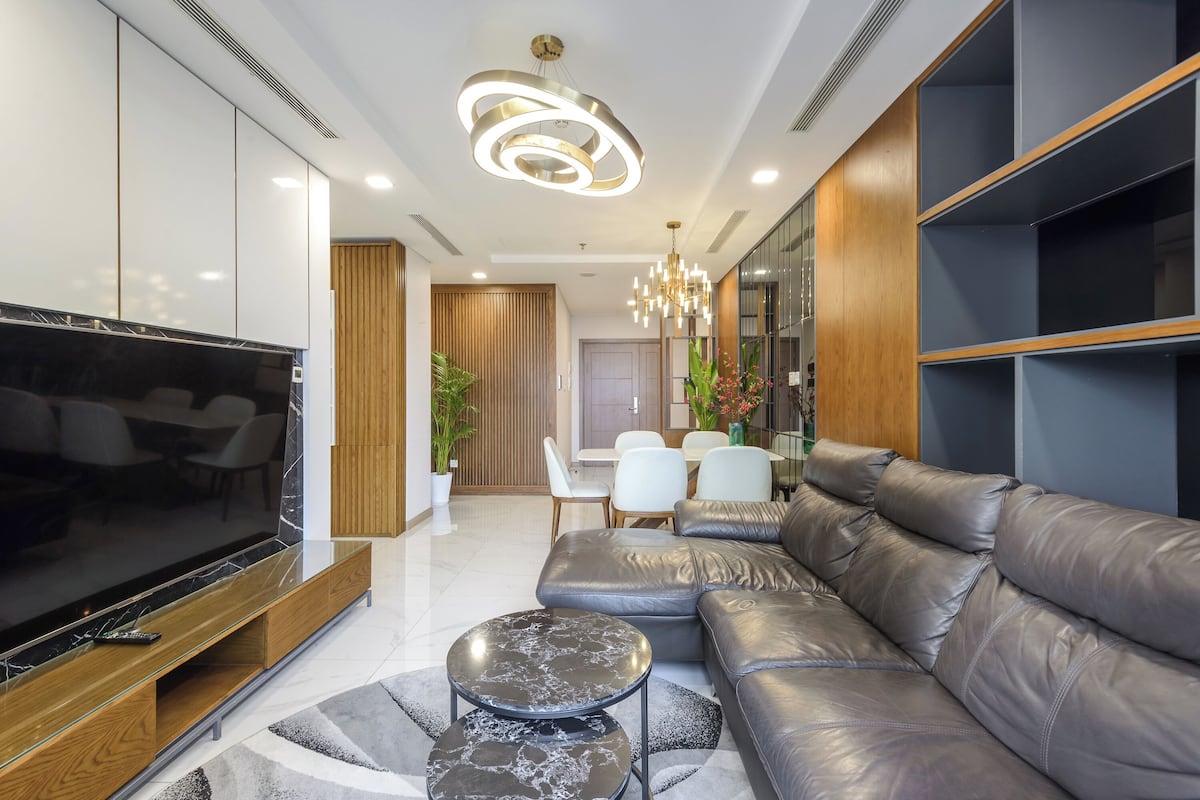 Uma sala de estar moderna com sofá seccional, televisão de tela plana e área de jantar com cadeiras brancas.