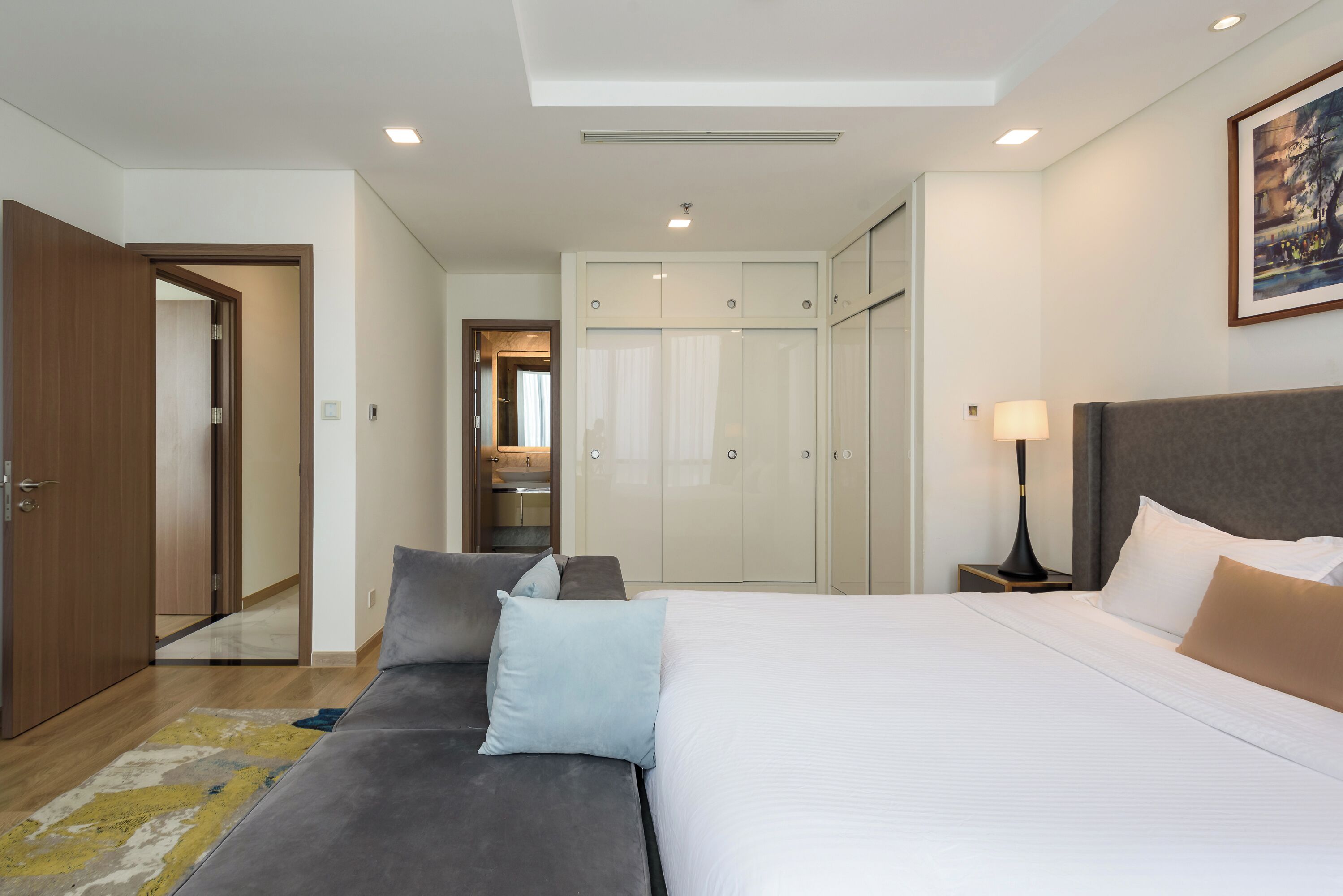 A modern hotel room with a large bed, a sofa, a wardrobe, and a mirror.