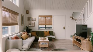 A living room with a sofa, coffee table, TV stand, and windows with blinds. - The Base Cabin A Frame - Your Gateway to Yosemite, Relaxation and Chill Vibes (Groveland)