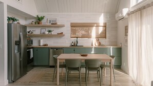 A modern kitchen with a dining area, featuring a wooden table, green chairs, and a built-in oven. - The Base Cabin A Frame - Your Gateway to Yosemite, Relaxation and Chill Vibes (Groveland)