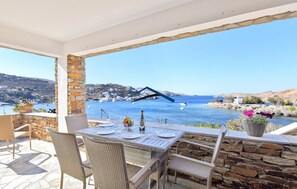 Terrassa amb taula preparada per dinar, amb vistes a la costa, un pont i vaixells.