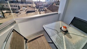 A balcony with a glass table and a chair, overlooking a cityscape with buildings and a clear sky. - Sea La Vie Seaview Apartment (Larnaca)