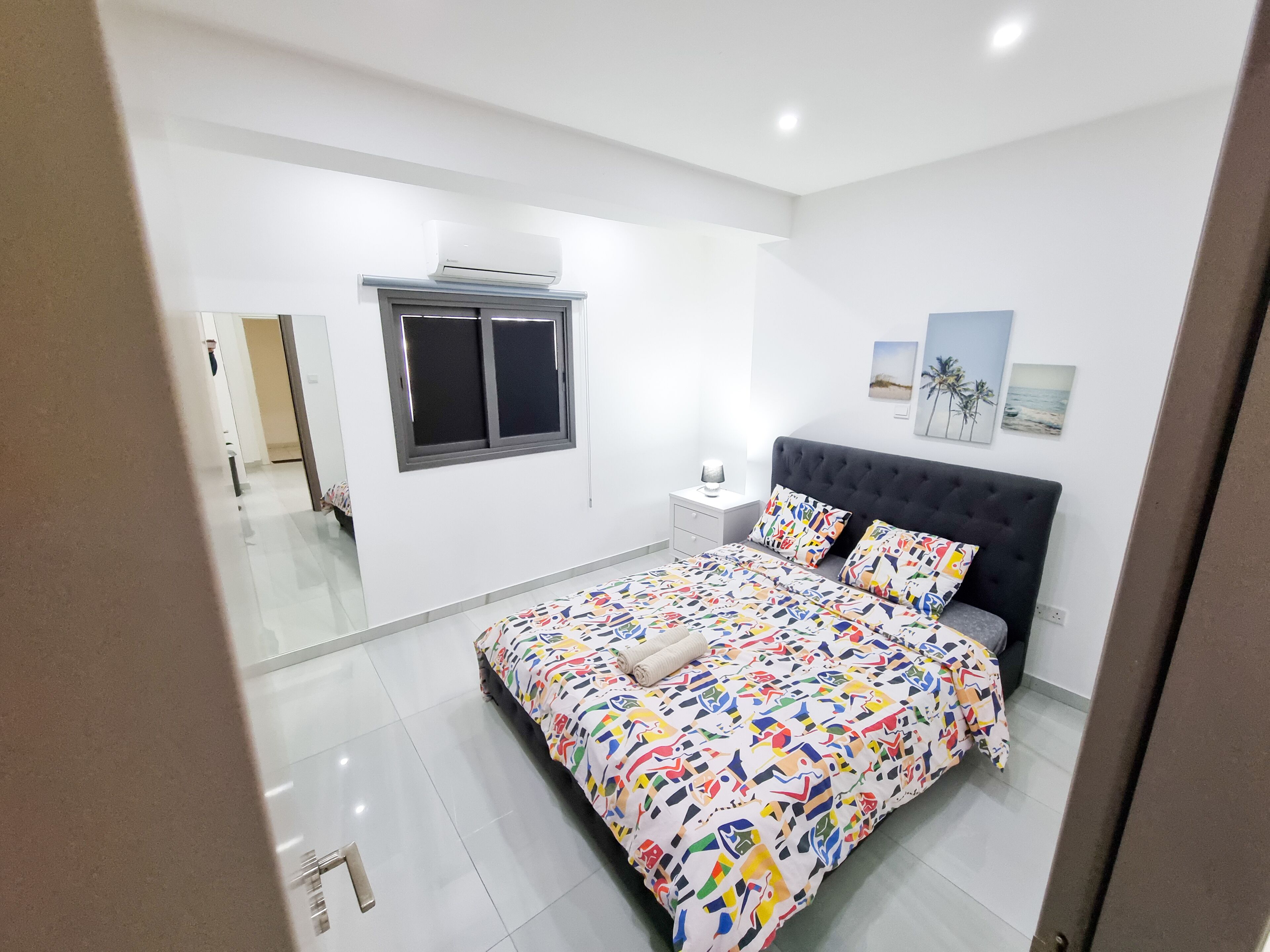 A bedroom with a bed, a window, a nightstand, and wall art.
