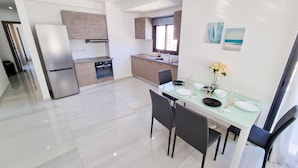 A modern kitchen with a refrigerator, oven, and dining table set with plates and glasses. - Sea La Vie Seaview Apartment (Larnaca)