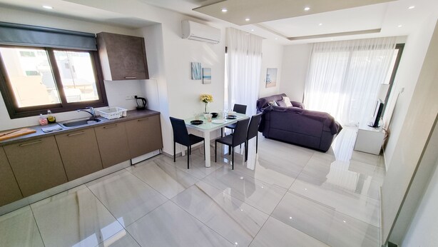 A modern kitchen with a dining area, a sofa, and a TV. - Sea La Vie Seaview Apartment (Larnaca)