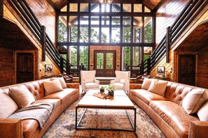 A spacious living room with leather sofas, a coffee table, and a large window offering a view of the outdoors.