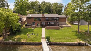 A two-story building with a deck and a view of a river. - Crystal Springs - Lakefront with Hot Tub! (Linn Creek)