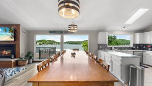 A spacious kitchen with a large island, a dining area with a wooden table, and a view of a lake through large windows. - Crystal Springs - Lakefront with Hot Tub! (Linn Creek)