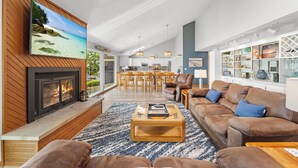 A spacious living room with a fireplace, a large flat-screen TV, a dining area, and a kitchen in the background. - Crystal Springs - Lakefront with Hot Tub! (Linn Creek)