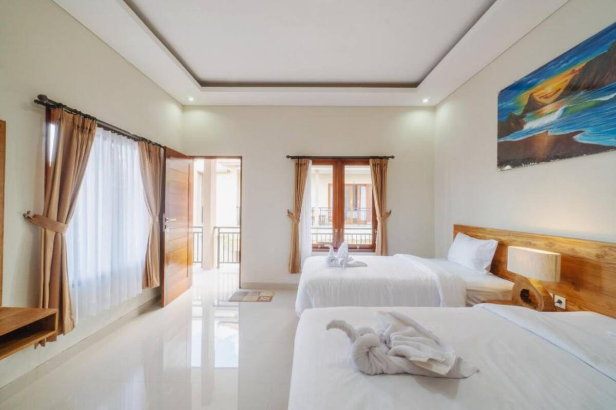 A hotel room with two beds, a painting on the wall, and a view of the outside.