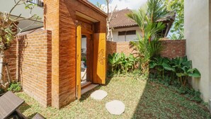 A brick house with a wooden door, a small garden with stepping stones, and a palm tree. - Komala Homestay by ecommerceloka (Canggu)