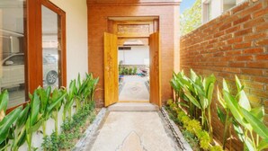 A narrow pathway leading to a building entrance, flanked by brick walls and green plants. - Komala Homestay by ecommerceloka (Canggu)