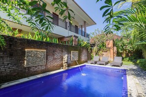 A swimming pool with a brick wall, a statue, and two lounge chairs. - Komala Homestay by ecommerceloka (Canggu)