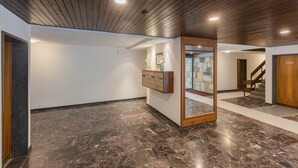 Un vestíbulo amplio con piso de mármol pulido, techo de madera y una recepción con un cuadro enmarcado.