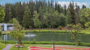 Un parque con un lago, árboles, una pista de atletismo y un puente al fondo.