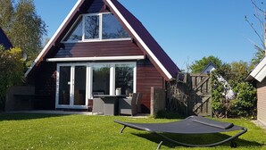 A modern house with a triangular roof, a patio with a table and chairs, and a lawn.