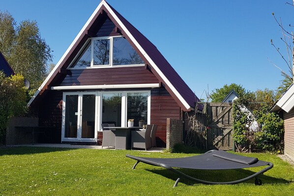 Una casa moderna con techo triangular, un patio con mesa y sillas, y un jardín.
