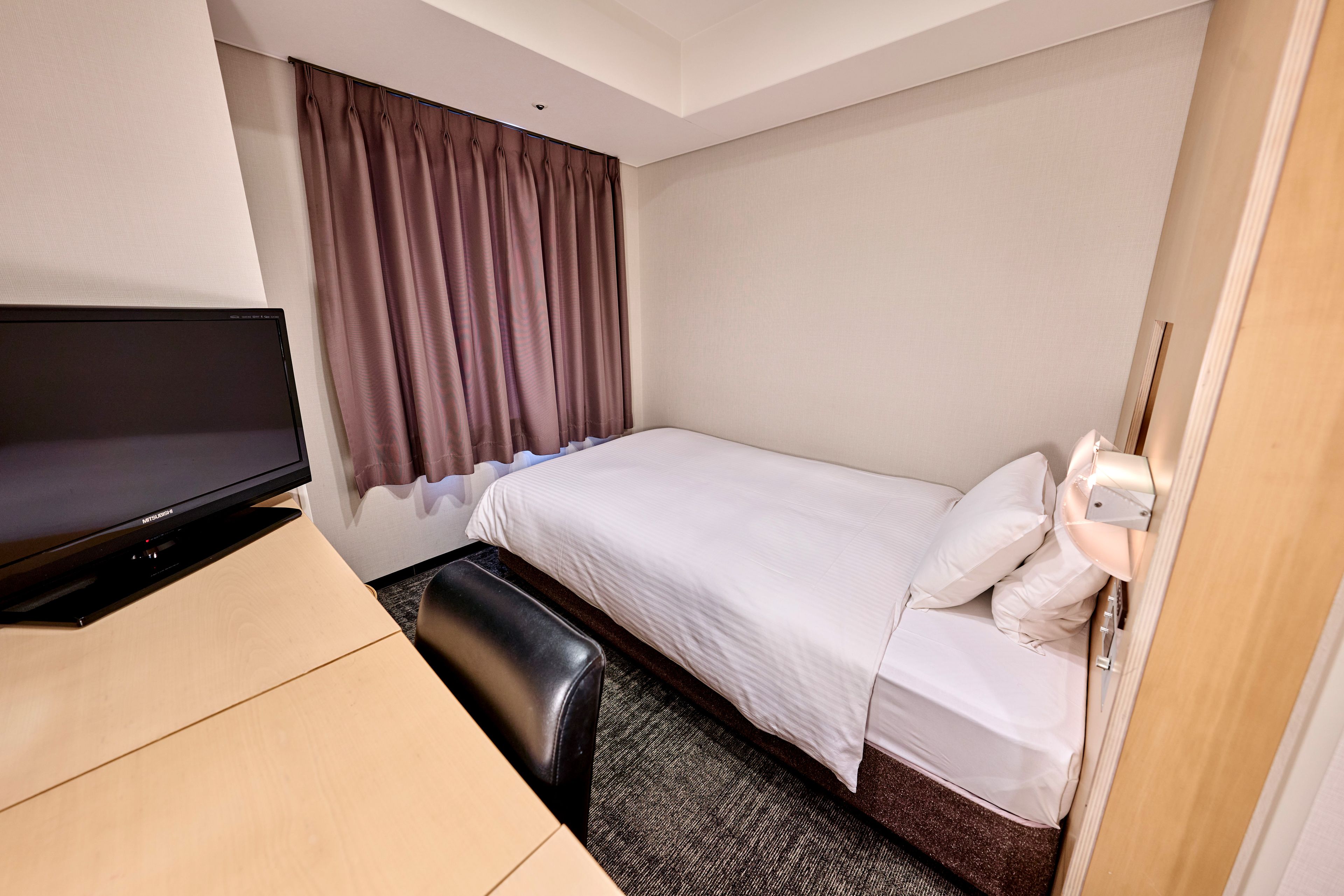 Ett hotellrum med en säng, ett skrivbord med en tv och ett fönster med gardiner.