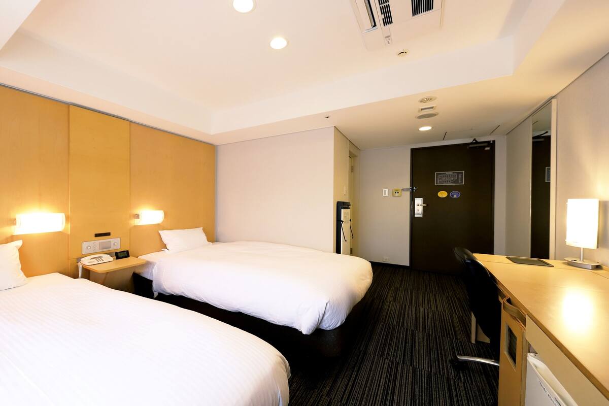 Une chambre d’hôtel avec deux lits, un bureau, une chaise et un miroir.