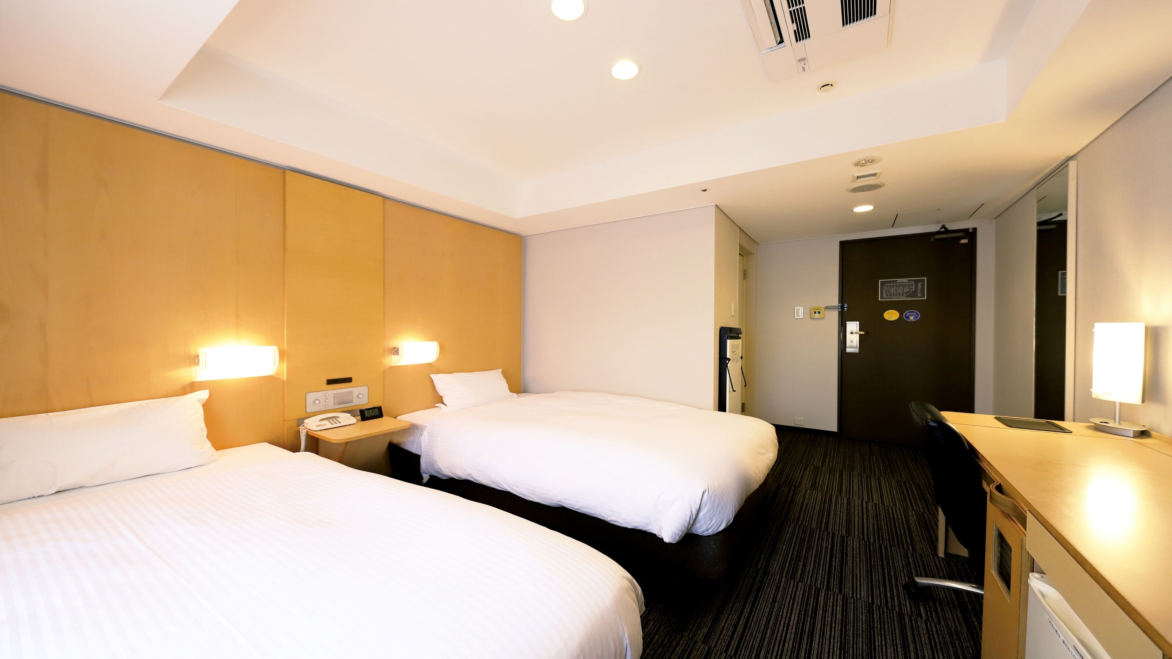 A hotel room with two beds, a desk, a chair, and a mirror.