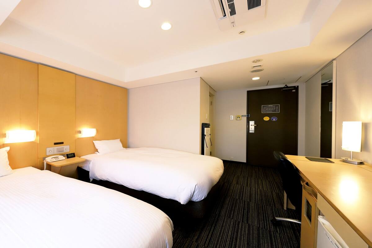 Une chambre d’hôtel avec deux lits, un bureau, une chaise et un miroir.