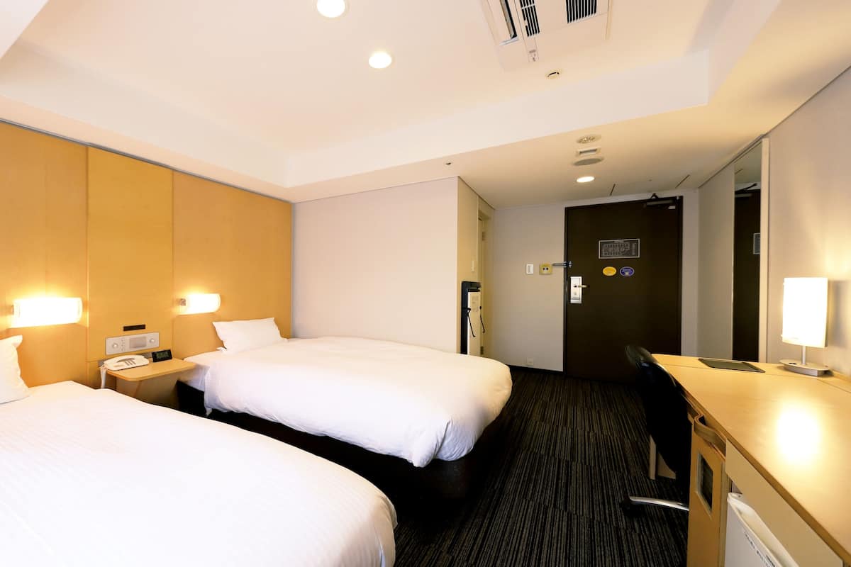 Ett hotellrum med två sängar, ett skrivbord, en stol och en spegel.