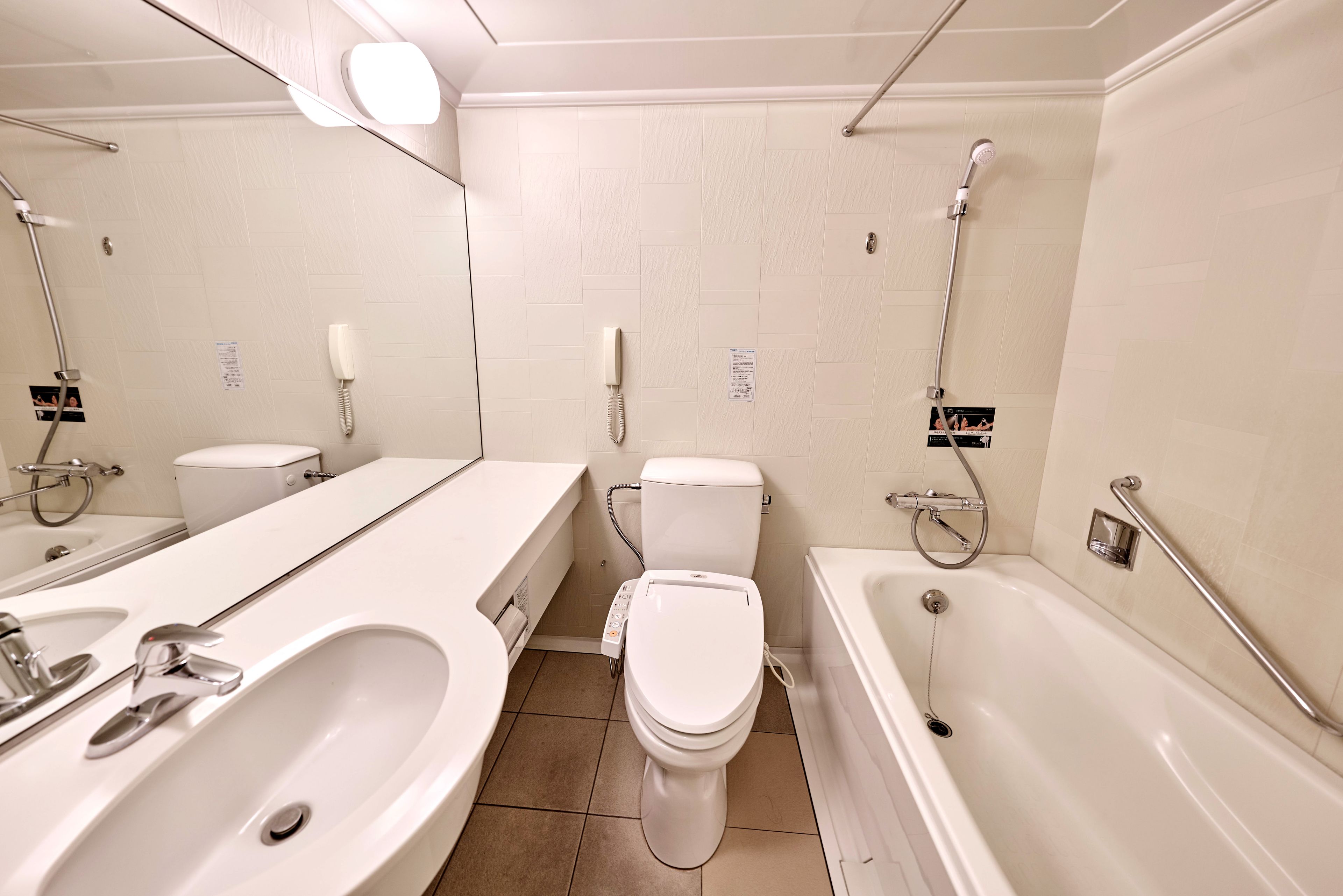 A modern bathroom with a large mirror, two sinks, a toilet, and a bathtub.