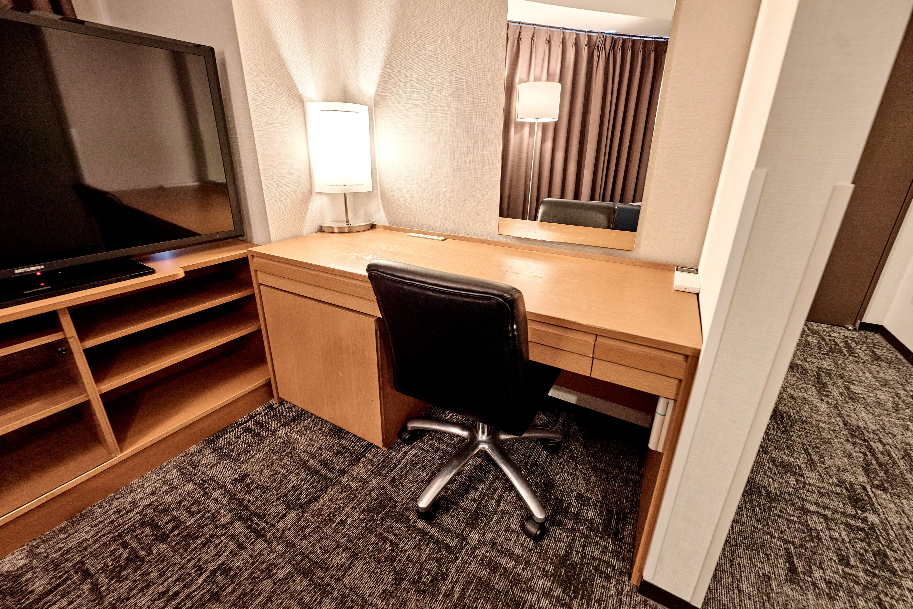 Una habitación de hotel con escritorio, silla, televisor, lámpara y espejo.