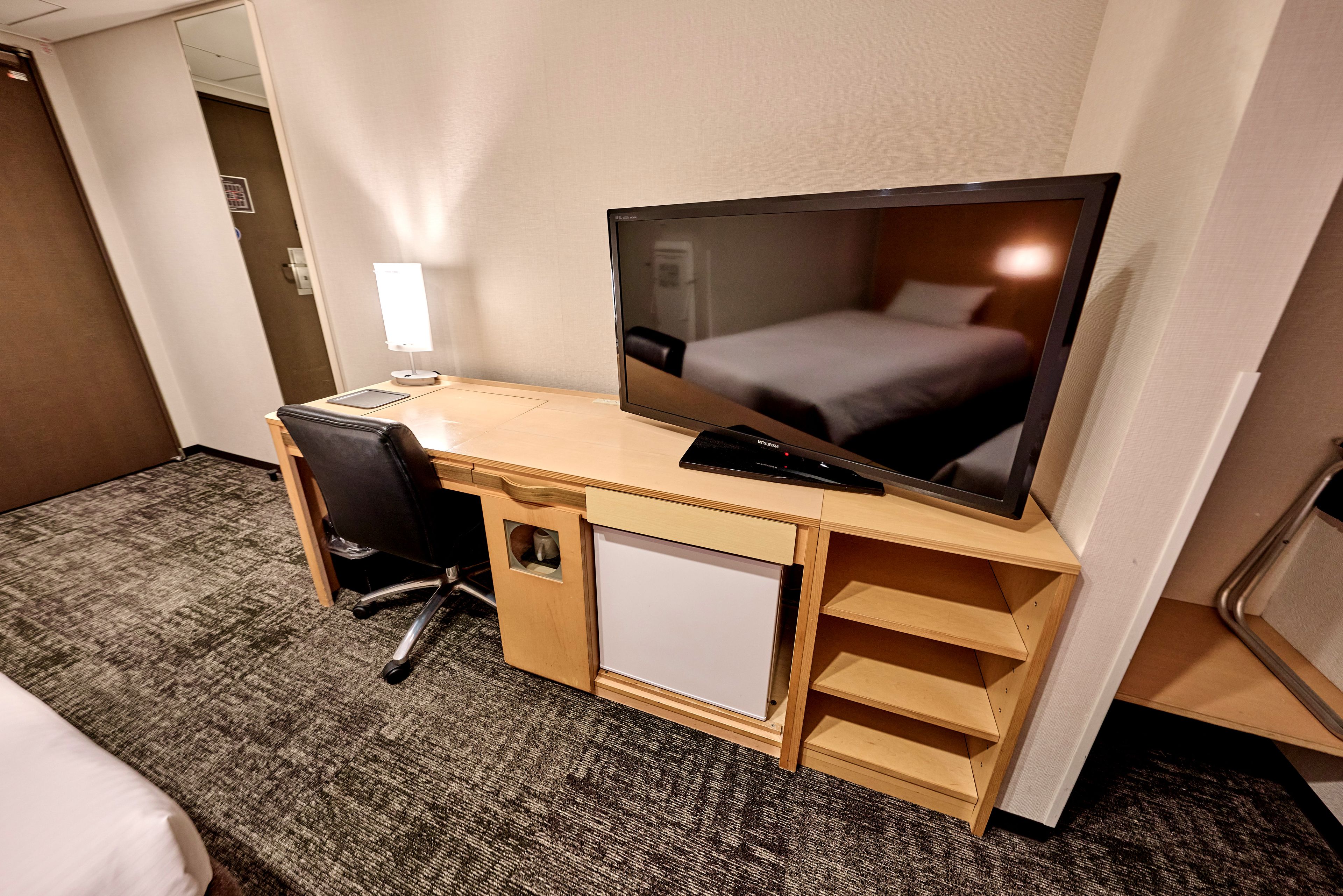 A hotel room with a desk, chair, television, and a bed.