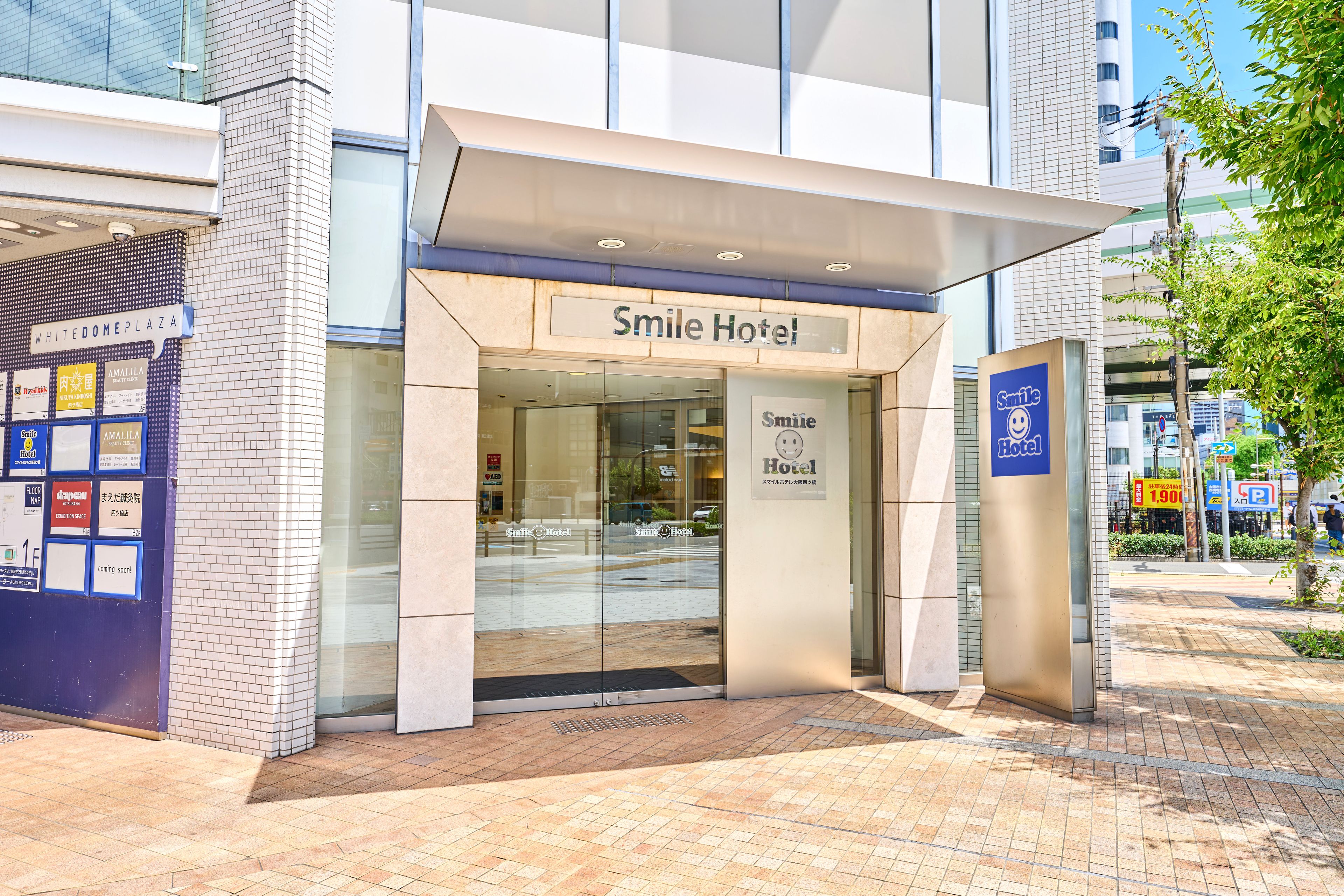 The exterior of the Smile Hotel with a clear entrance, a signboard, and a tiled pavement.