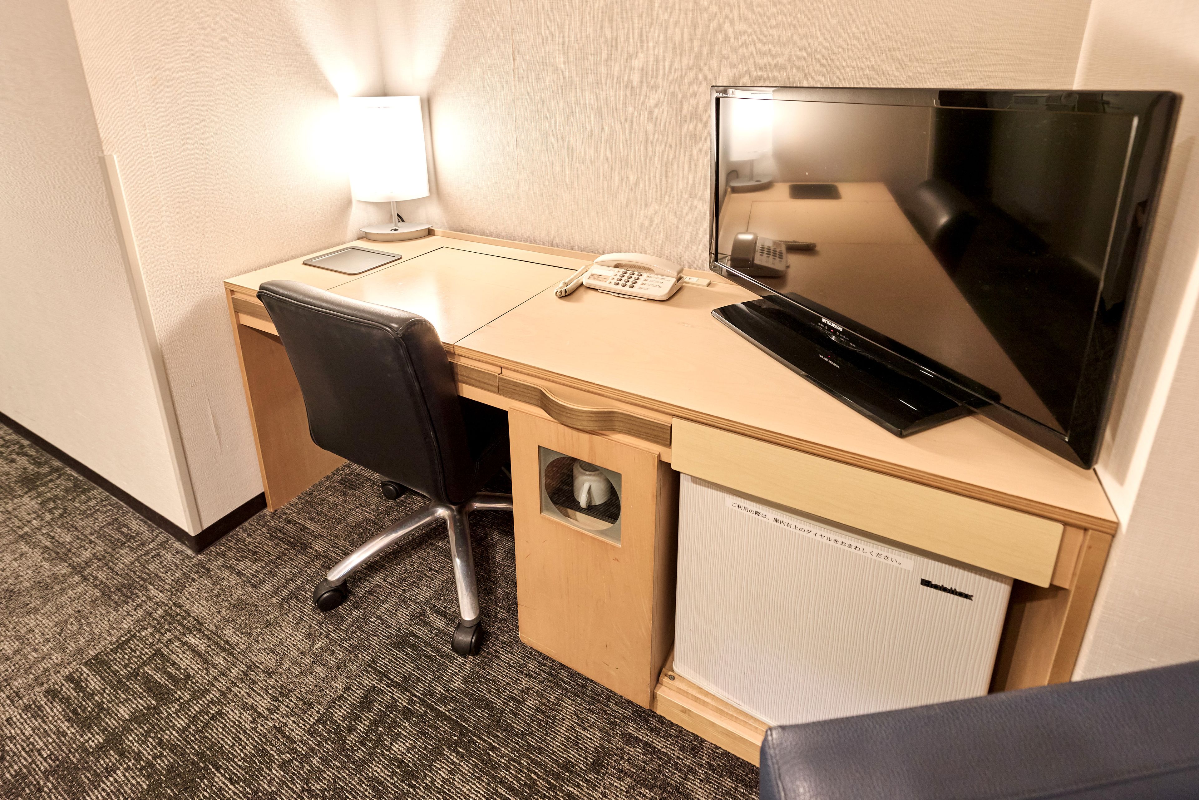 Une chambre d’hôtel équipée d’un bureau, d’une chaise, d’une lampe, d’un téléphone, d’une télévision et d’un radiateur.
