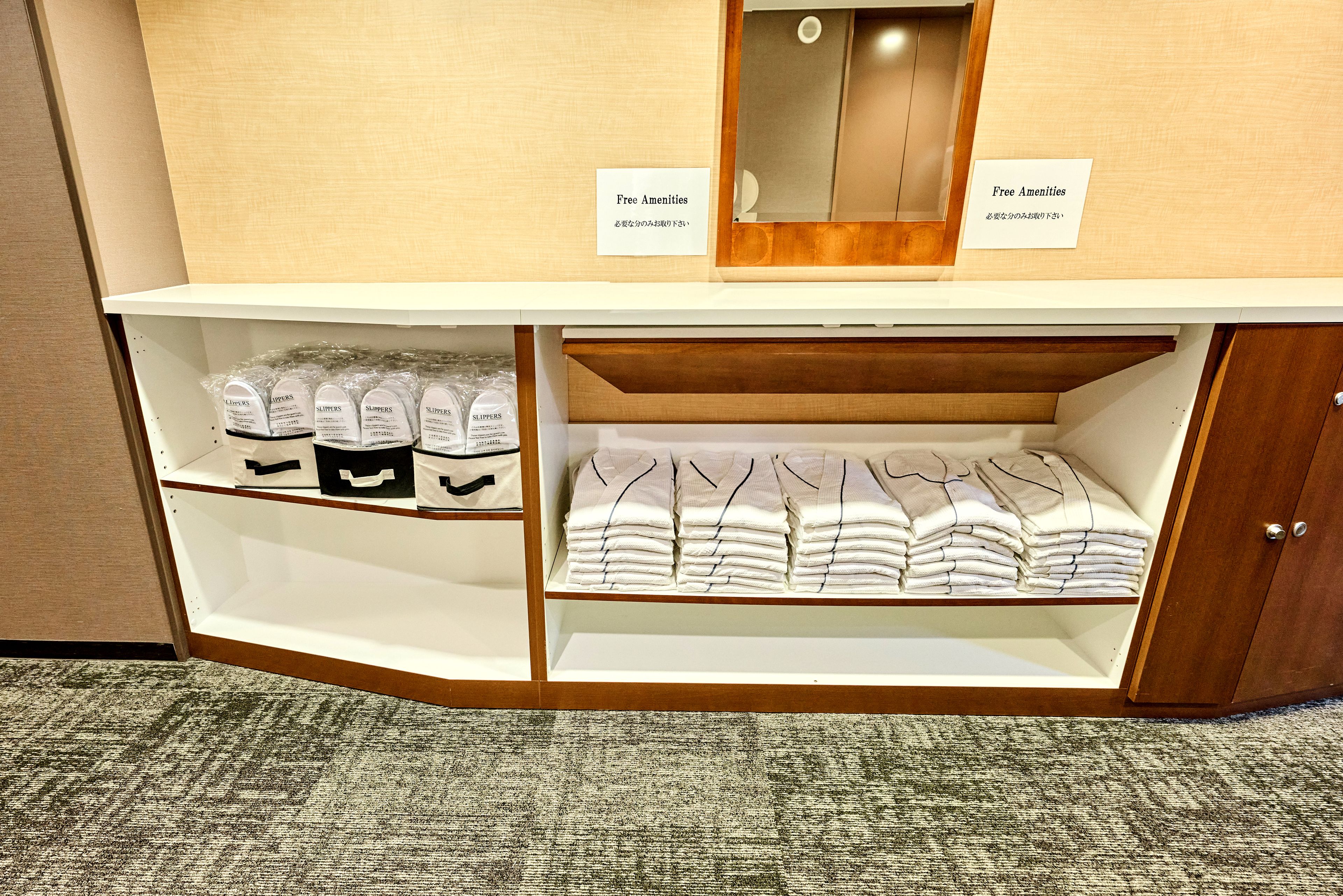 A hotel room with a vanity area containing slippers and towels.