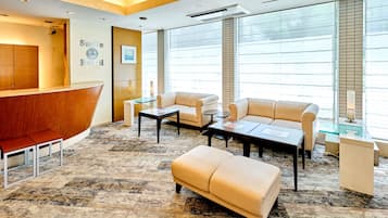 A hotel reception area with a wooden reception desk, a sofa, a coffee table, and a patterned carpet.