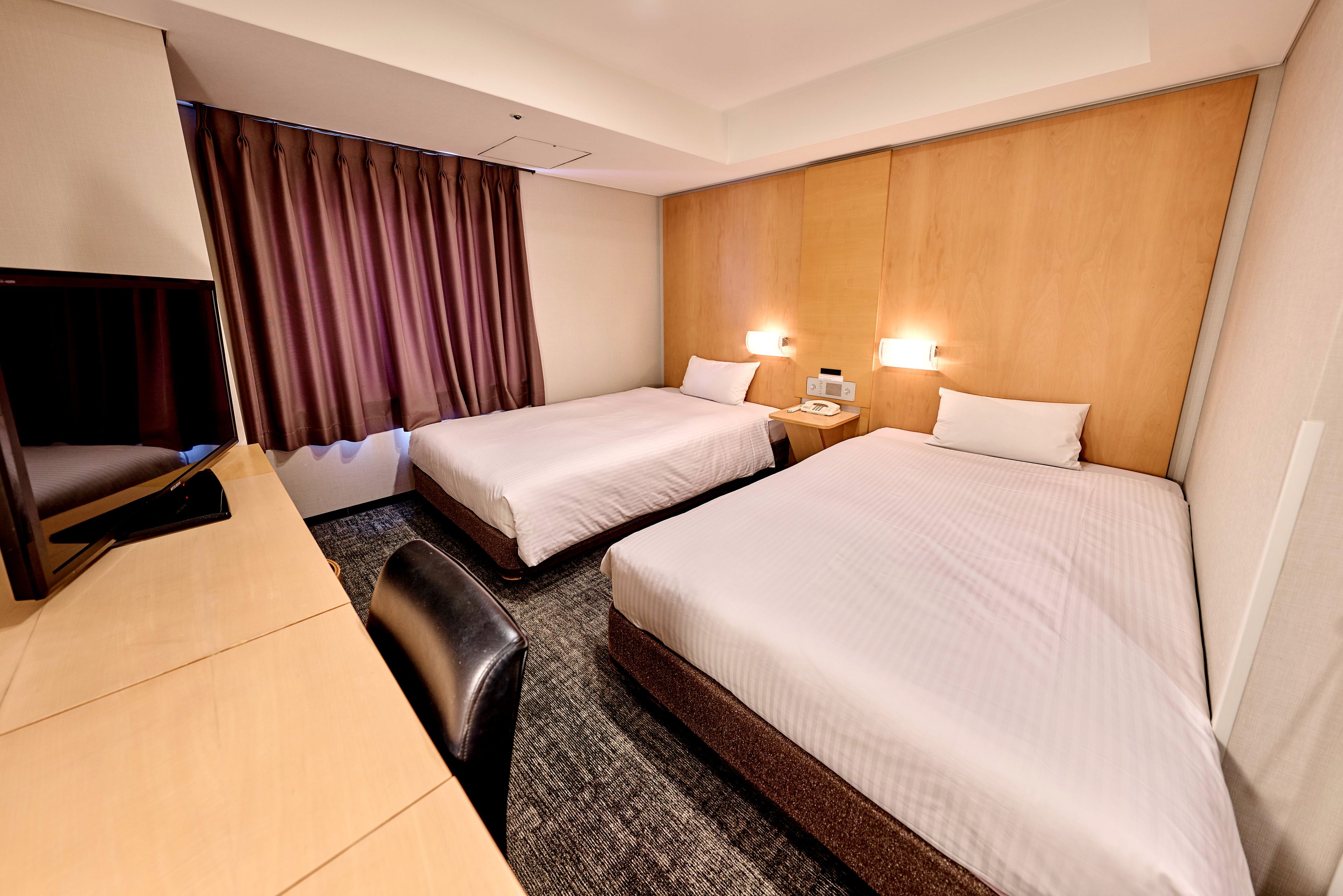 A hotel room with two beds, a desk, a chair, a TV, and a curtain.