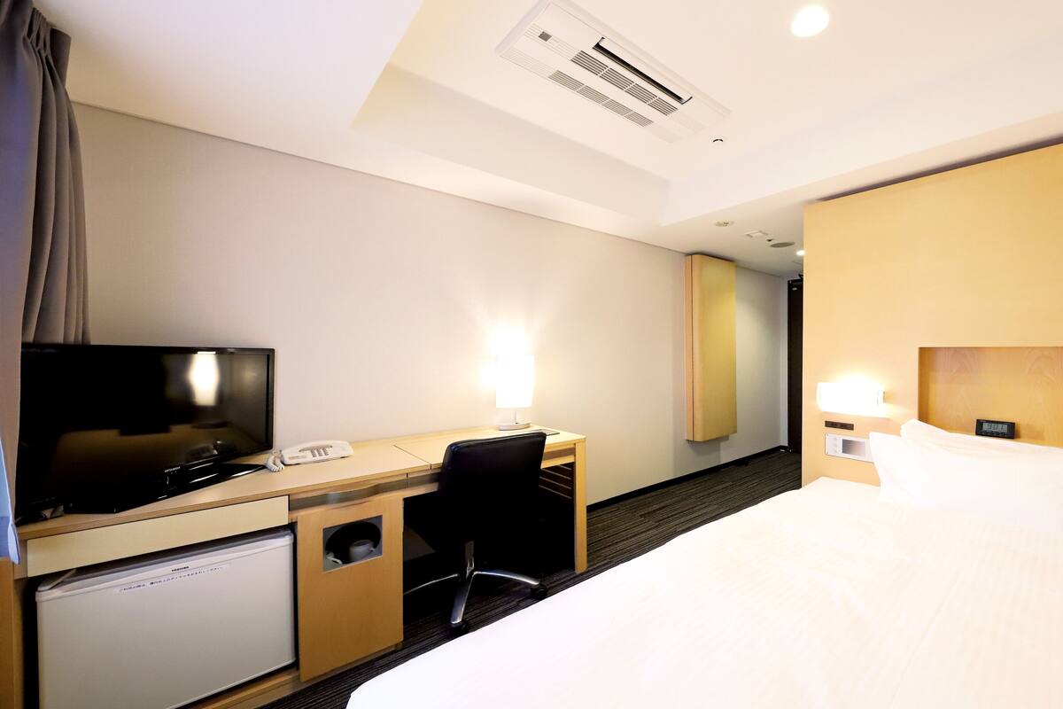 Une chambre d’hôtel équipée d’un lit, d’un bureau, d’une chaise, d’une télévision, d’un téléphone et d’un petit réfrigérateur.