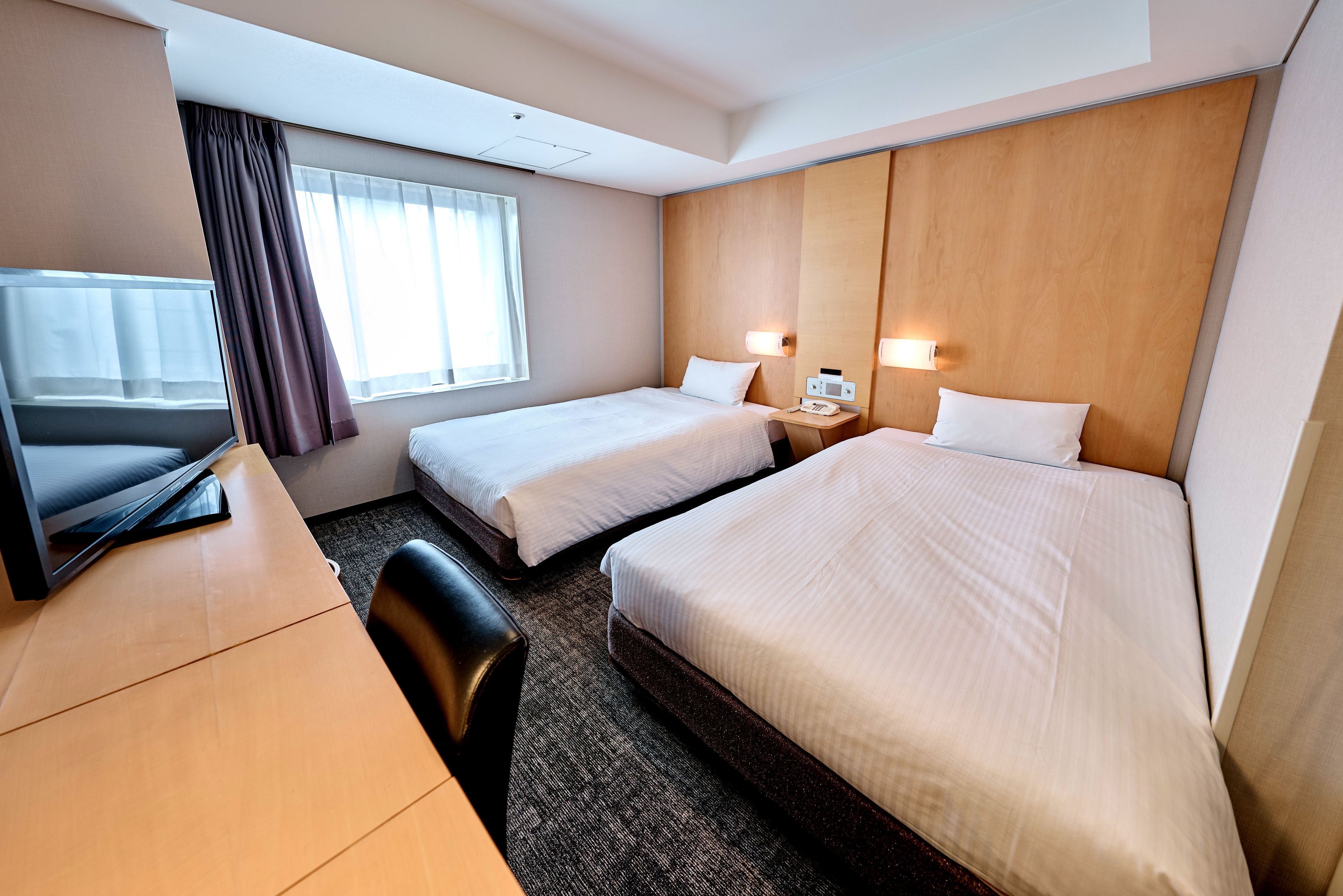 Ein Hotelzimmer mit zwei Betten, einem Schreibtisch, einem Stuhl und einem Fernseher.