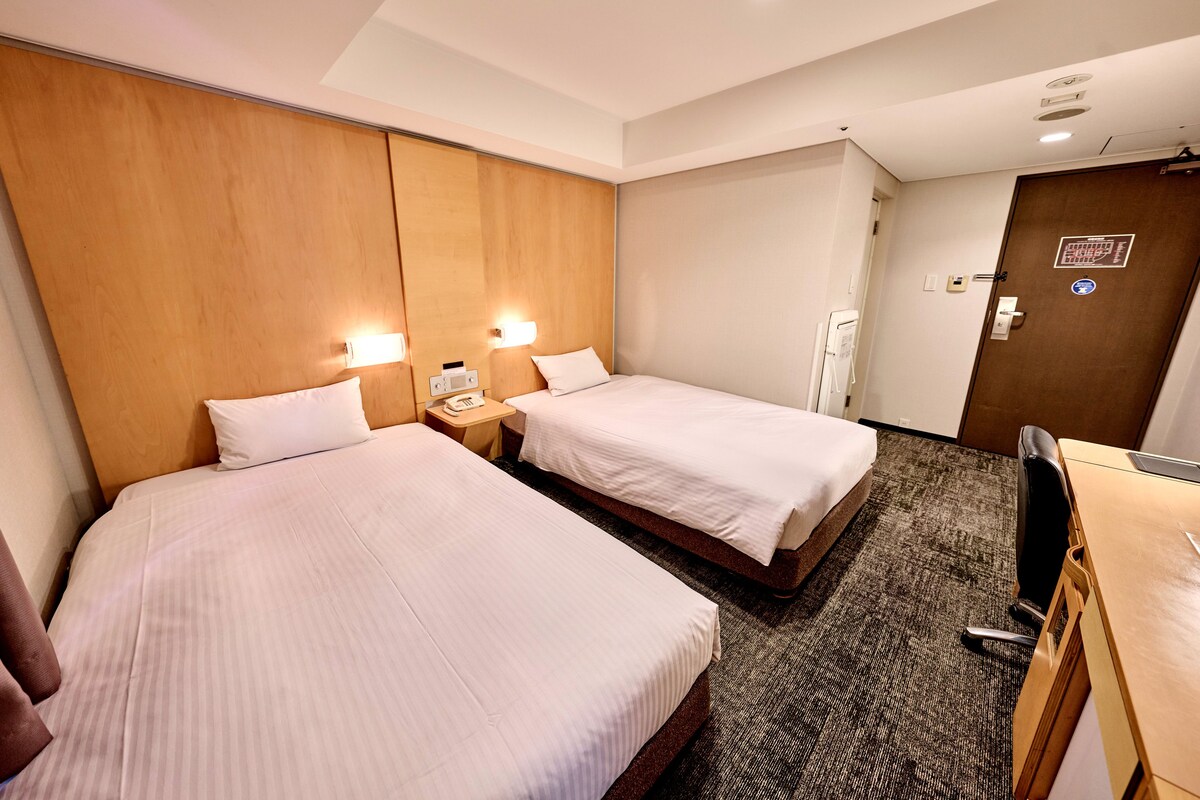 Ein Hotelzimmer mit zwei Betten, einem Schreibtisch und einer Tür.