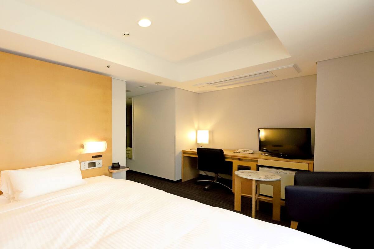 Une chambre d’hôtel équipée d’un lit, d’un bureau, d’une chaise, d’une télévision et d’une petite table.