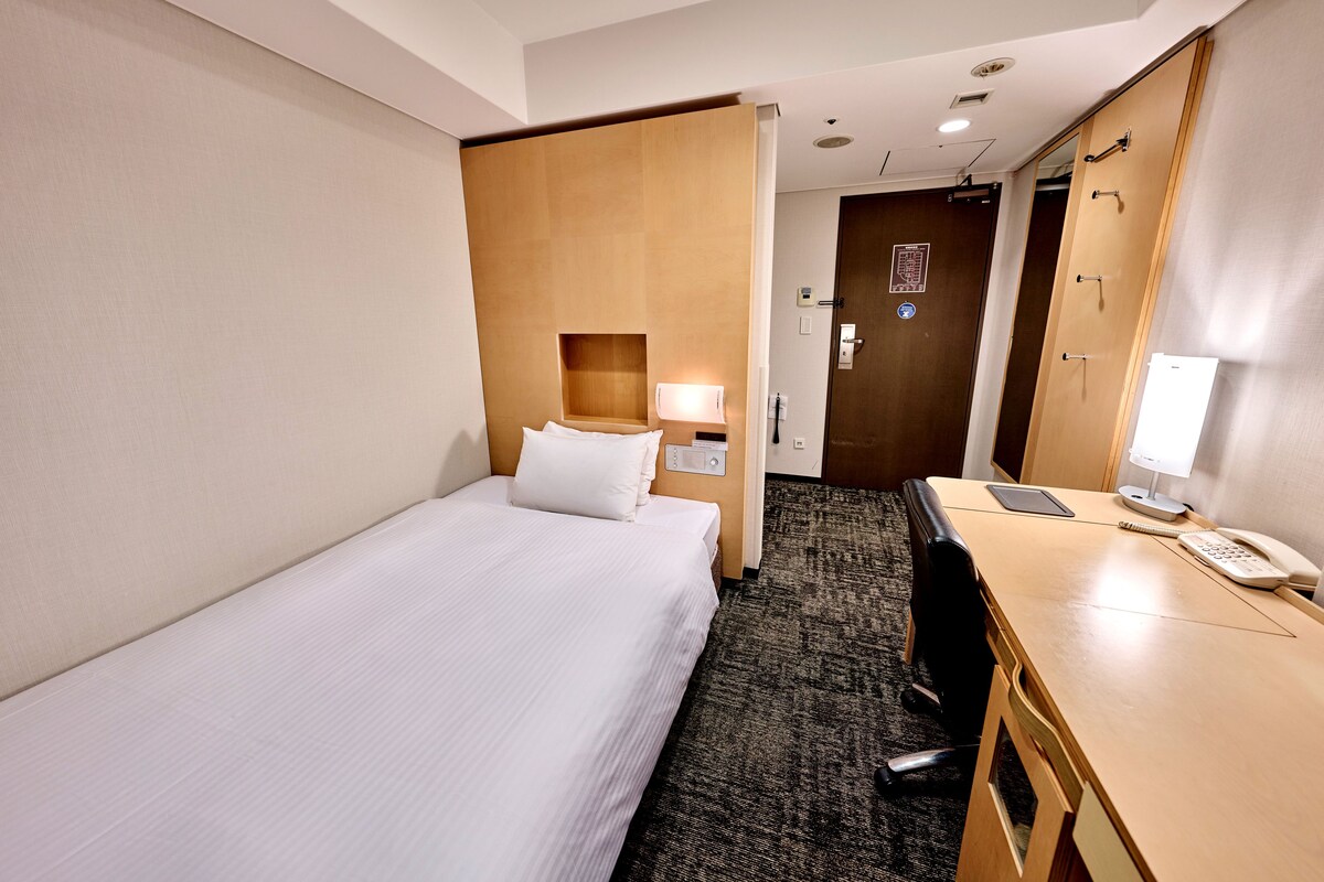 Ein Hotelzimmer mit einem Einzelbett, einem Schreibtisch mit Telefon und einem Spiegel.