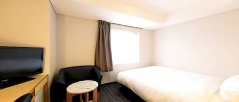 A hotel room with a bed, a TV, a small table, and a window with curtains.