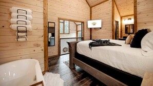 A wooden cabin bedroom with a bed, a small desk, a chair, and a mirror. - Cozy Modern Farmhouse Hot Tub, Firepit, Game Table (Broken Bow)